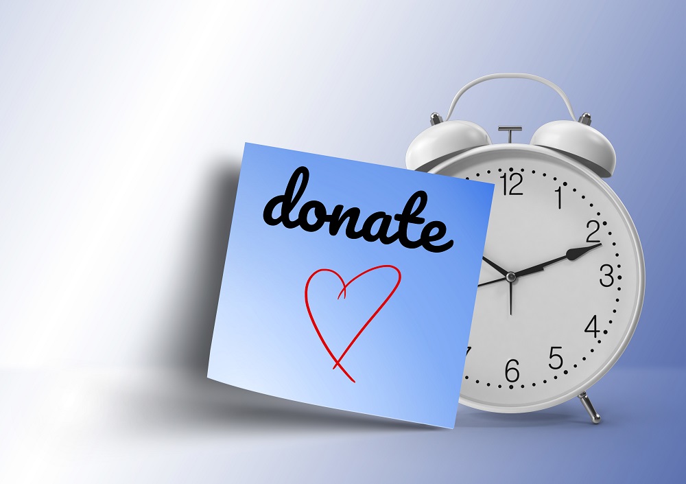 handwrited donate message on blue sticky note paper attached on white alarm clock with large copy space